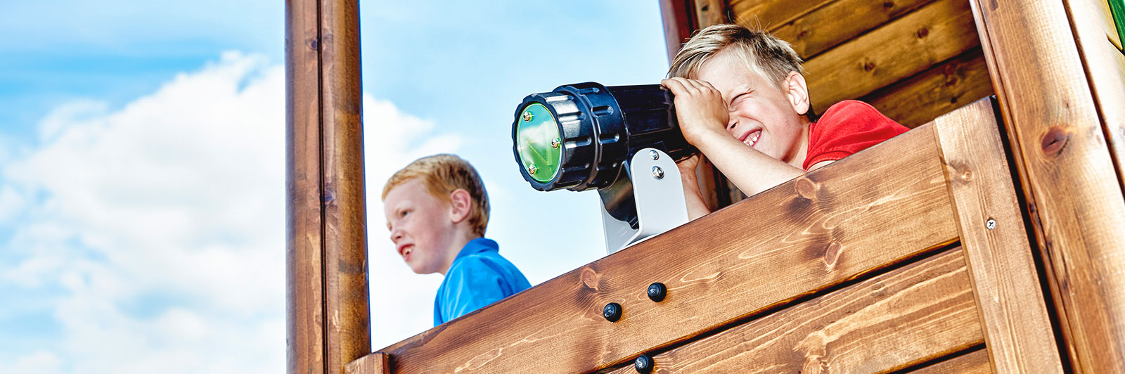 Un jeune garçon regarde à travers un télescope situé au sommet d'une grande aire de jeux en bois.